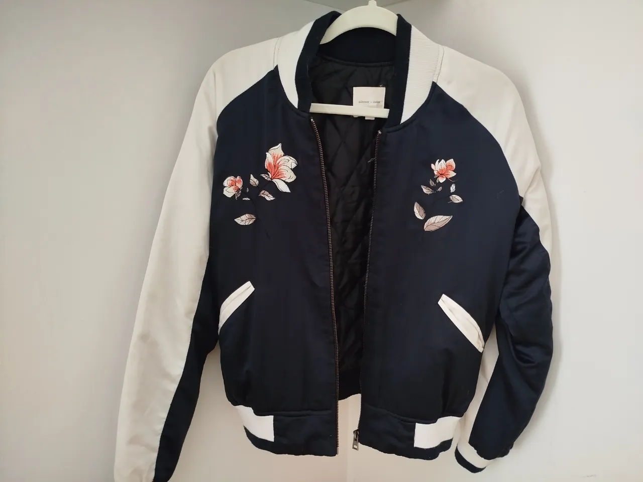 Campera bomber de mujer, azul marino con mangas blancas. Detalles florales bordados en la parte delantera y trasera. Ideal para un look casual y moderno.