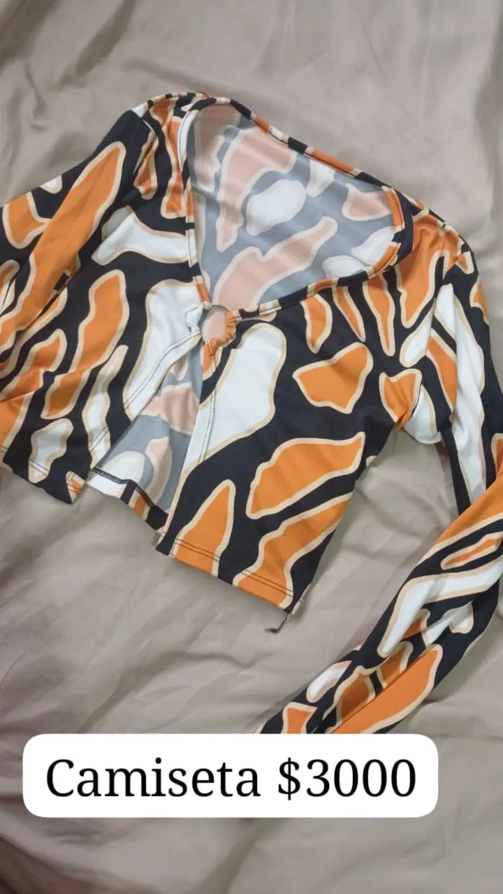 Remera manga larga con estampa abstracta en naranja, blanco y negro. Posee un detalle de aro en el escote y un corte en la parte delantera. Ideal para un look canchero y moderno.