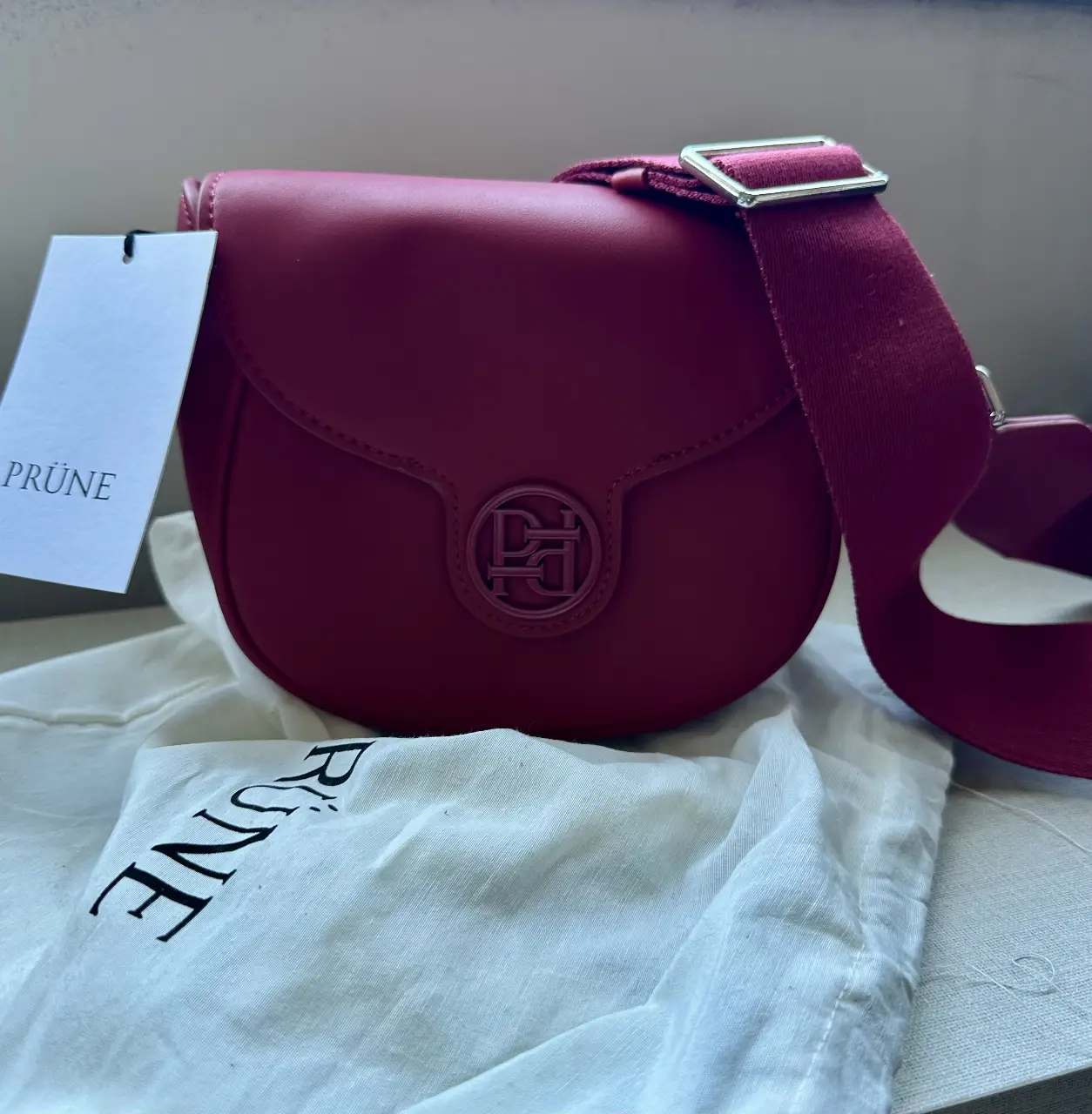 Bandolera PRÜNE de cuero sintético color rojo, con correa ajustable y cierre de solapa. Ideal para un look casual y moderno.