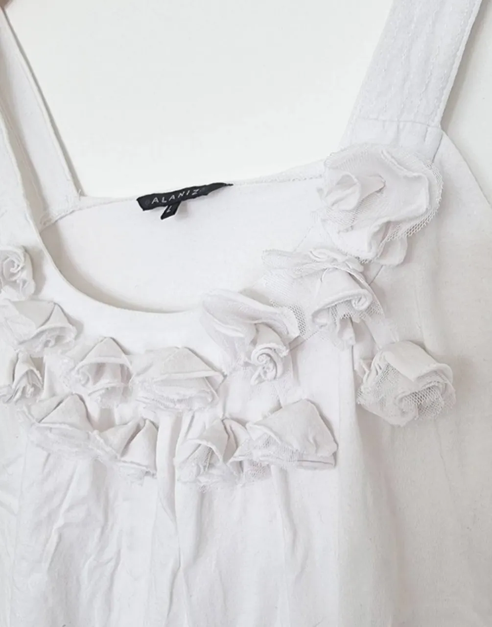 Musculosa blanca con delicados detalles de flores y volados en el escote. Perfecta para un look fresco y femenino.