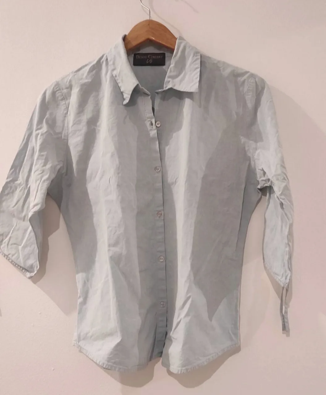 Camisa manga 3/4 color celeste pastel, con botones al frente y detalle de lazos en los puños. Ideal para un look casual y fresco.