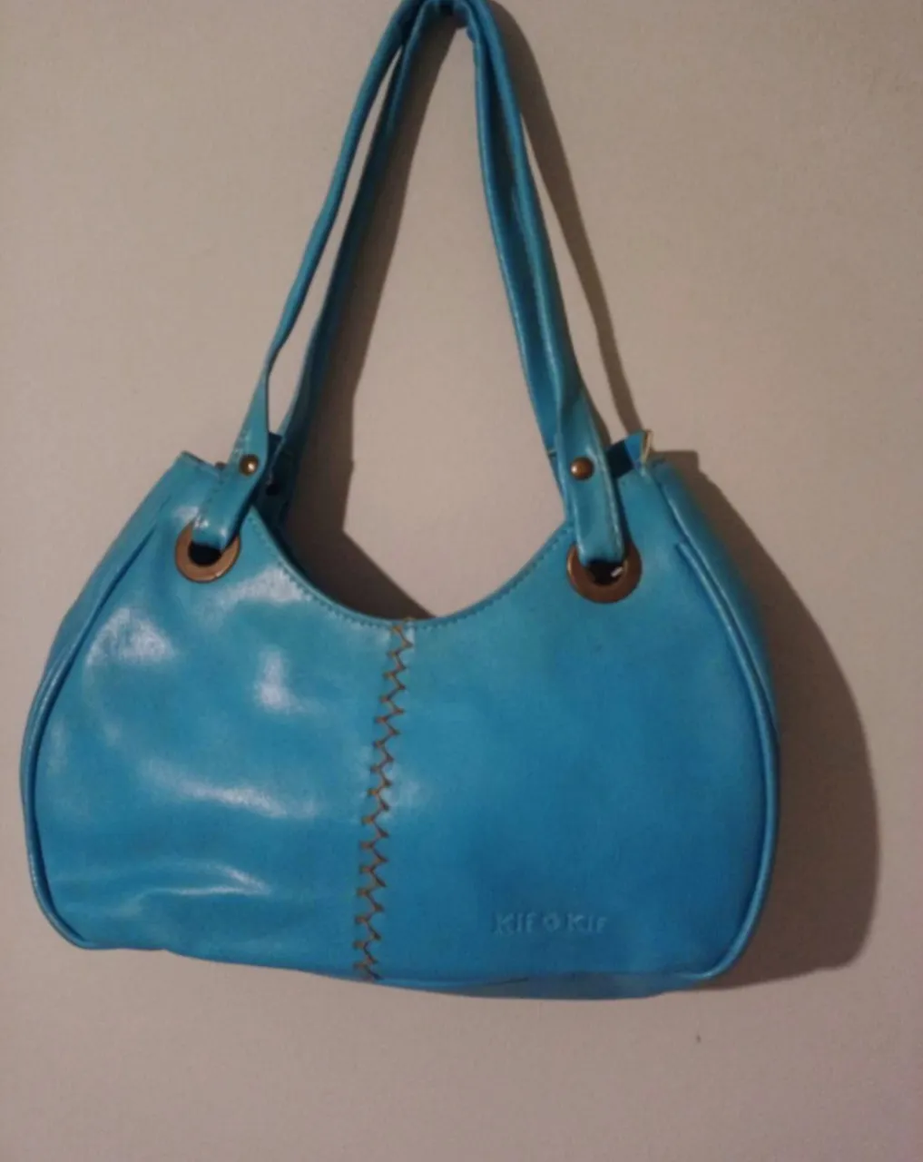 Bolso turquesa vibrante, con costuras decorativas en el frente y detalles metálicos en las asas. Un accesorio chic y moderno para elevar cualquier look.