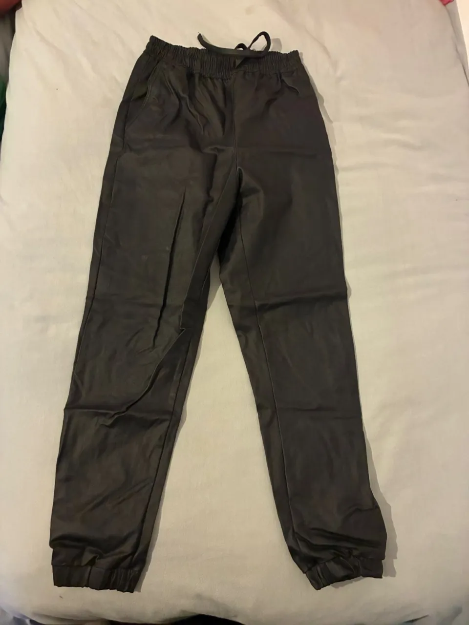 Pantalón de mujer, estilo jogger, confeccionado en cuero sintético negro. Posee cintura elastizada con cordón para un ajuste perfecto y puños en los tobillos. Ideal para un look casual y moderno.
