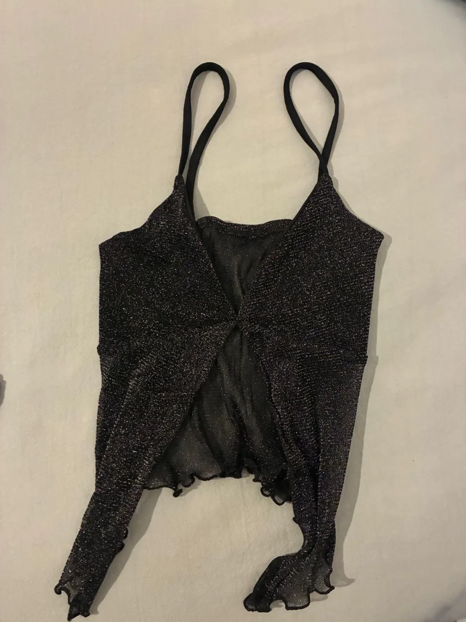 Top negro con brillos, ideal para fiesta o salida. Diseño con tirantes finos y detalle drapeado. Perfecto para un look moderno y audaz.
