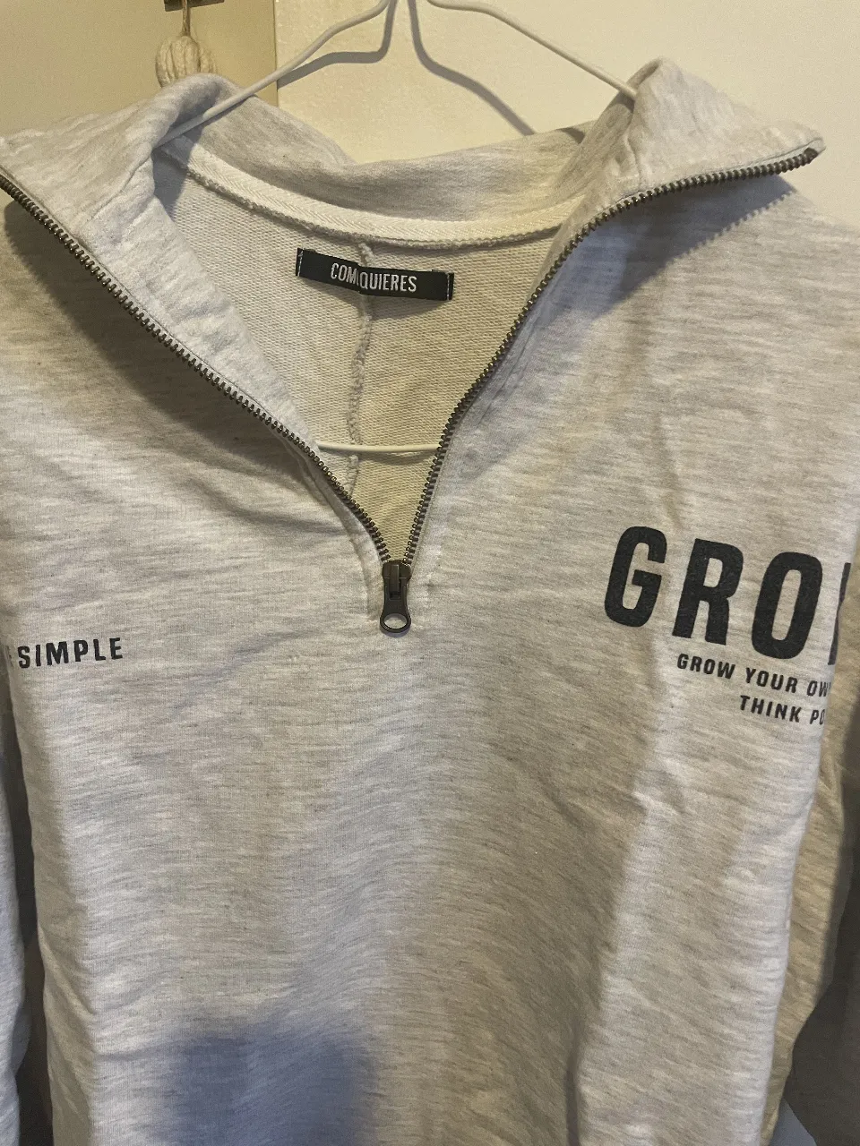 Buzo con cierre y cuello alto para mujer. Diseño con la palabra "GROW" estampada en negro y la frase "GROW YOUR OWN THINK POSITIVE". Ideal para un look casual y cómodo.