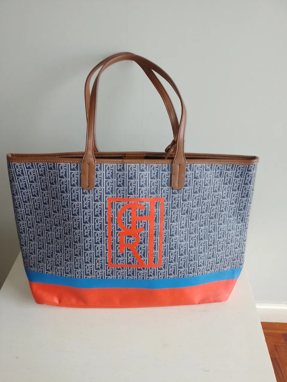 ¡Impresionante tote bag de gran tamaño, perfecta para llevar todo lo que necesitás! Con un diseño monograma en azul y blanco, y detalles vibrantes en naranja y azul en la base. Incluye un práctico neceser a juego. Ideal para el día a día, escapadas de fin de semana o para ir a la playa.