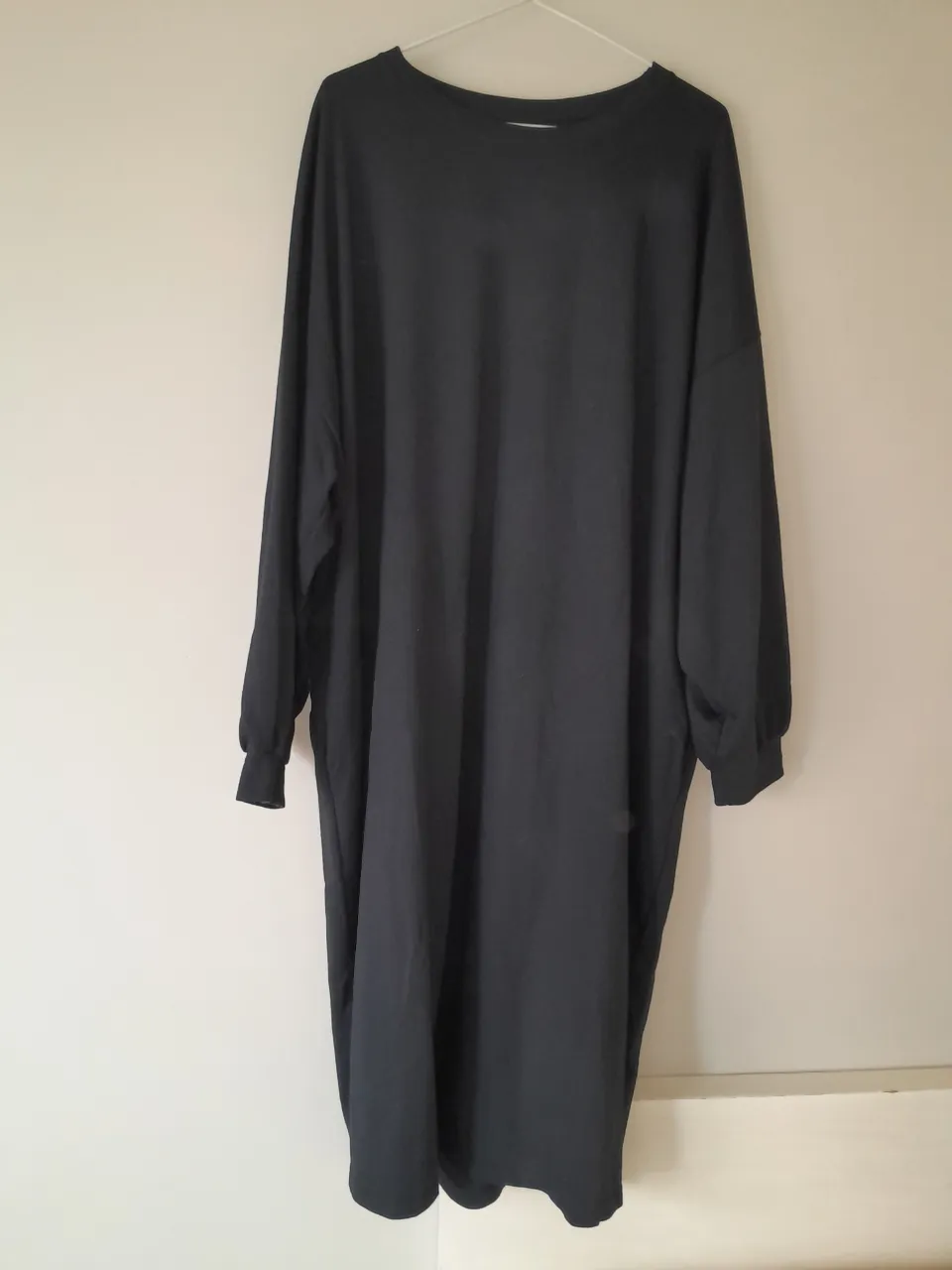 Vestido negro de manga larga con un pequeño detalle de corazón rosa y blanco en la parte superior de la espalda.