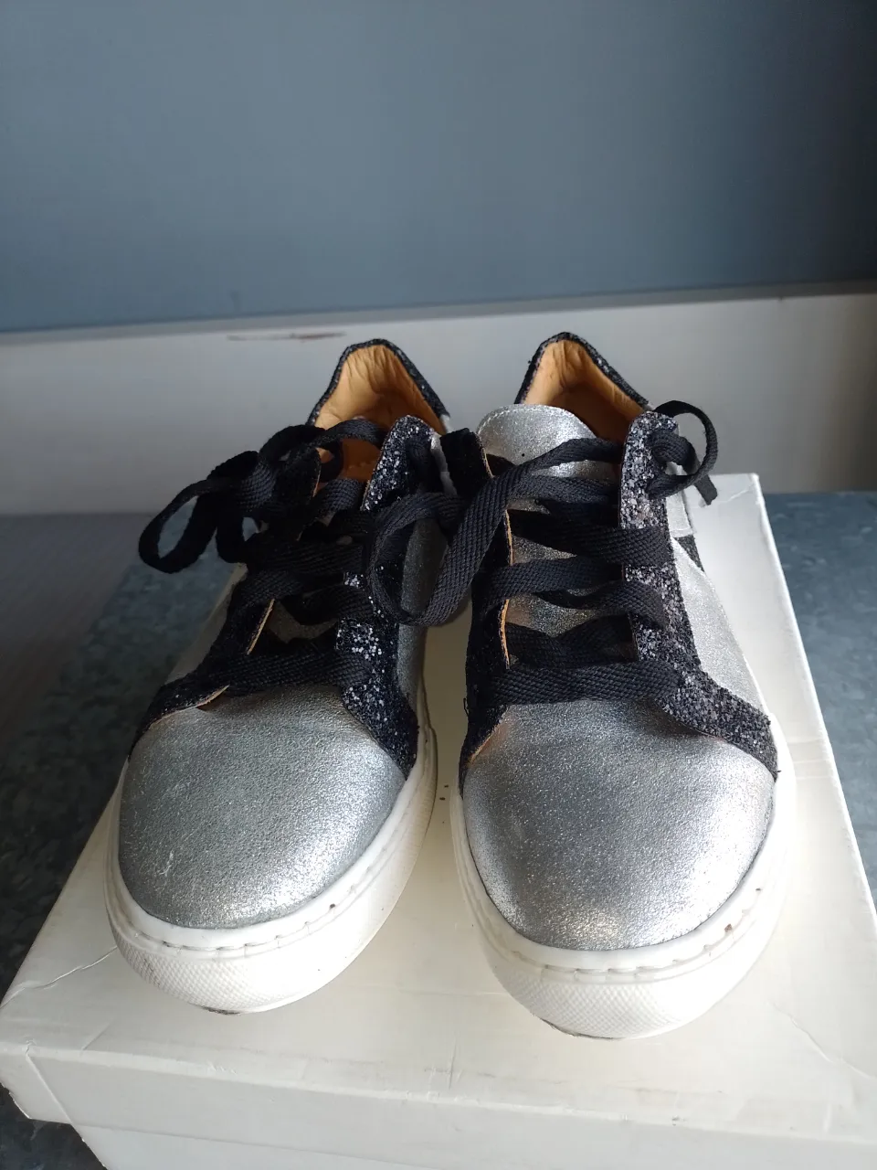 Zapatillas plateadas con detalles de glitter negro y estrella lateral. Cordones negros. Ideales para un look canchero y moderno.