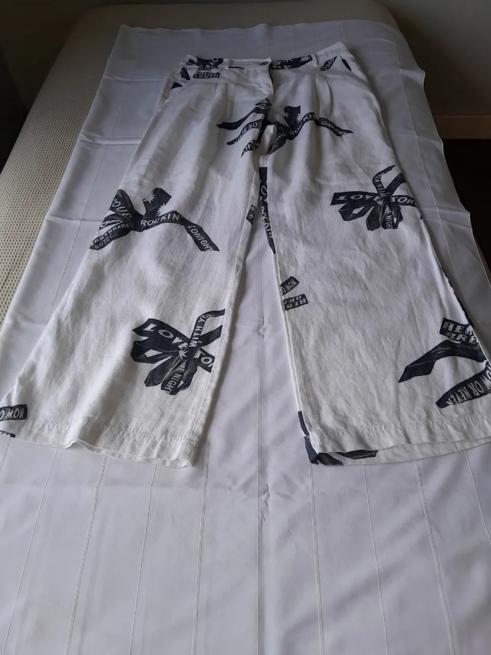 Pantalón blanco con estampa de cintas negras con inscripciones. Tiene dos bolsillos delanteros y dos traseros.