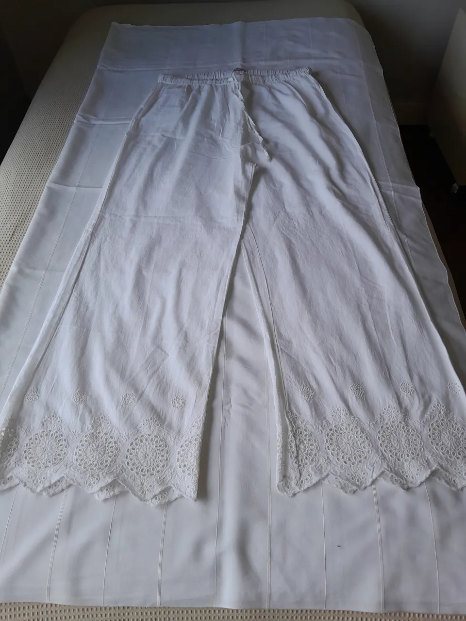 Pantalón blanco de tela liviana con detalles de bordado y puntilla en los ruedos. Cintura elastizada con cordón.