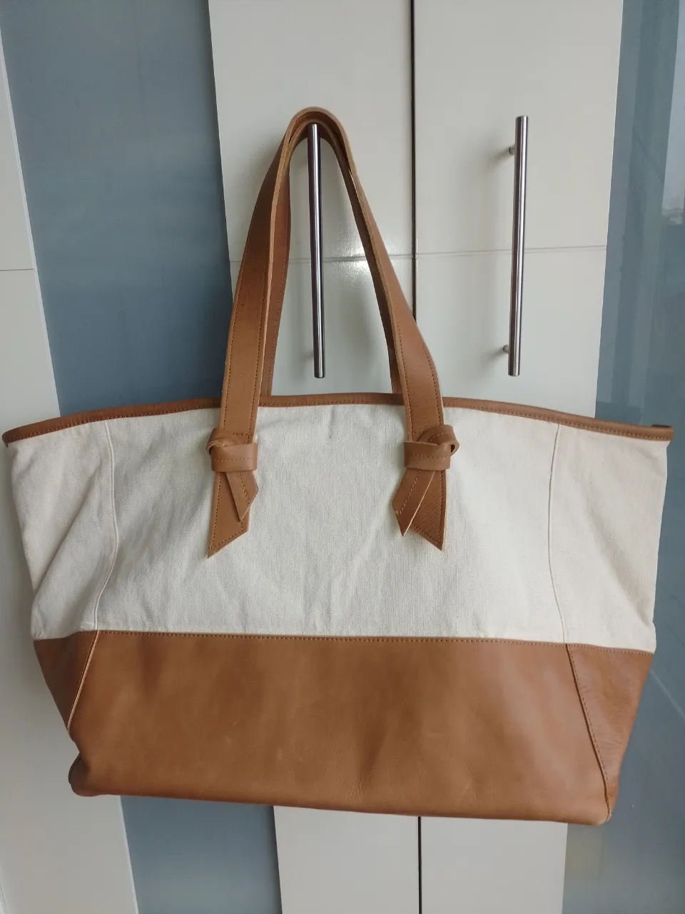 Bolsón de lona color crudo con detalles y base de cuero marrón. Ideal para el día a día, viajes cortos o para llevar todo lo que necesitás. Amplio y práctico.