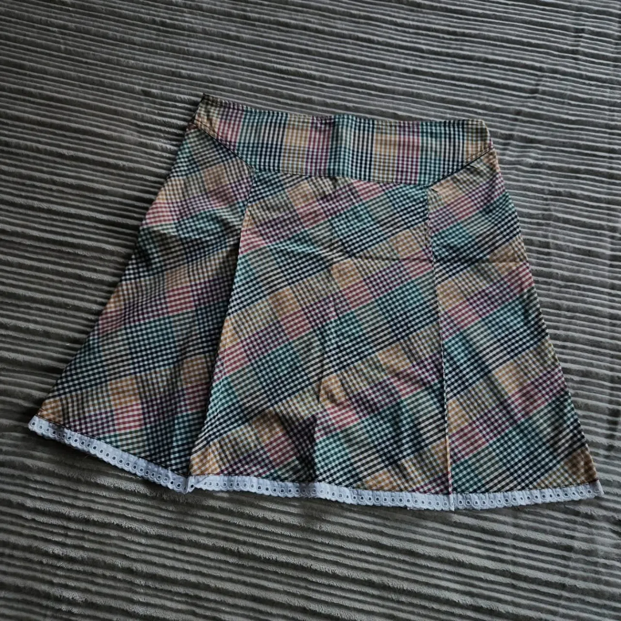 Pollera corta a cuadros escoceses en tonos verdes, marrones, rojos y negros. Posee un detalle de puntilla blanca en el ruedo. Tela fresca de camisa. Dice talle L, perova para un S