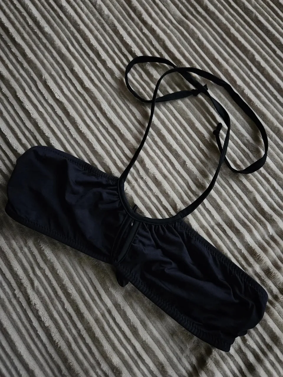 Top de bikini negro, estilo corpiño, con tiras para atar en cuello y espalda. Posee detalle de fruncido en la parte superior y un lazo en la parte delantera.