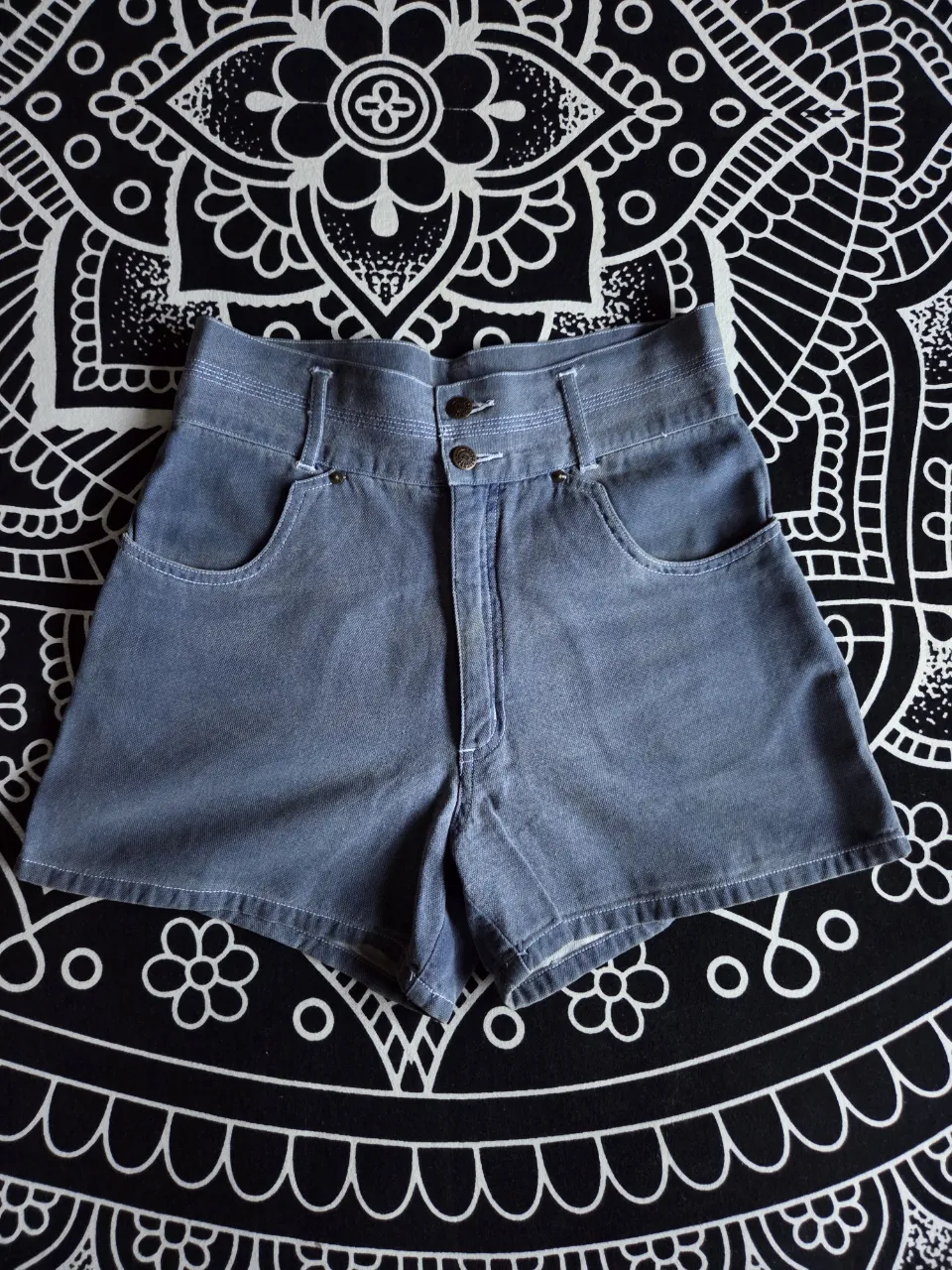 Shorts de jean rigido liviano, tiro alto, color azul desgastado. Posee dos bolsillos delanteros y dos traseros. Cierre con dos botones en la parte frontal. Traido de Brasil, vintage.