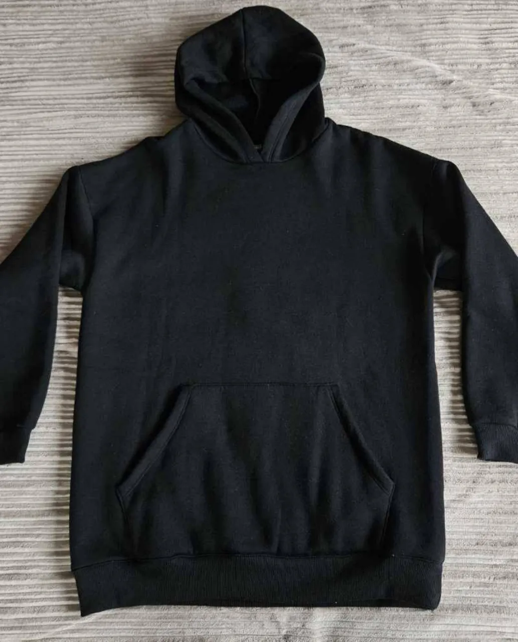 Buzo negro oversize con capucha y bolsillo canguro delantero.