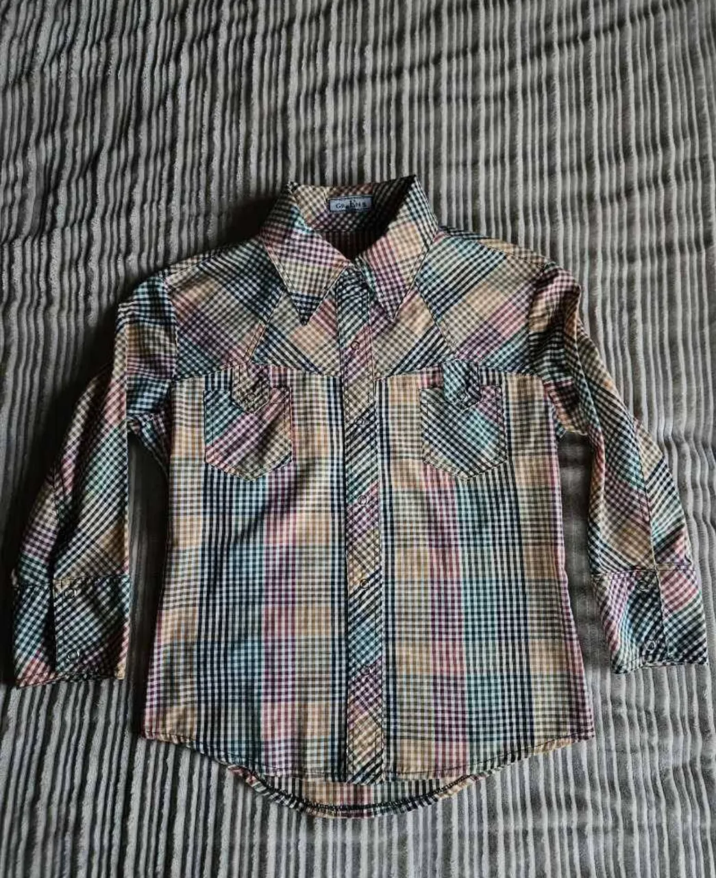 Camisa a cuadros de manga 3/4 con cuello clásico y dos bolsillos en el frente. Posee botones a presión.