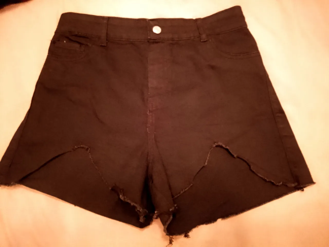 Shorts de jean negros con roturas irregulares en el ruedo. Tiro alto, con bolsillos y detalles de costura.tiene un ojal de atrás descocido
