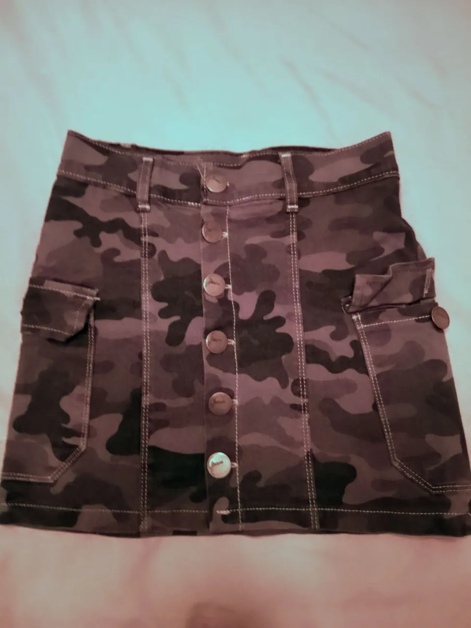 Pollera de jean con estampa camuflada, tiro alto y detalles de bolsillos cargo. elastizada. Posee botones al frente y un corte moderno ideal para looks urbanos y cancheros.Dice talle 38 pero es XS