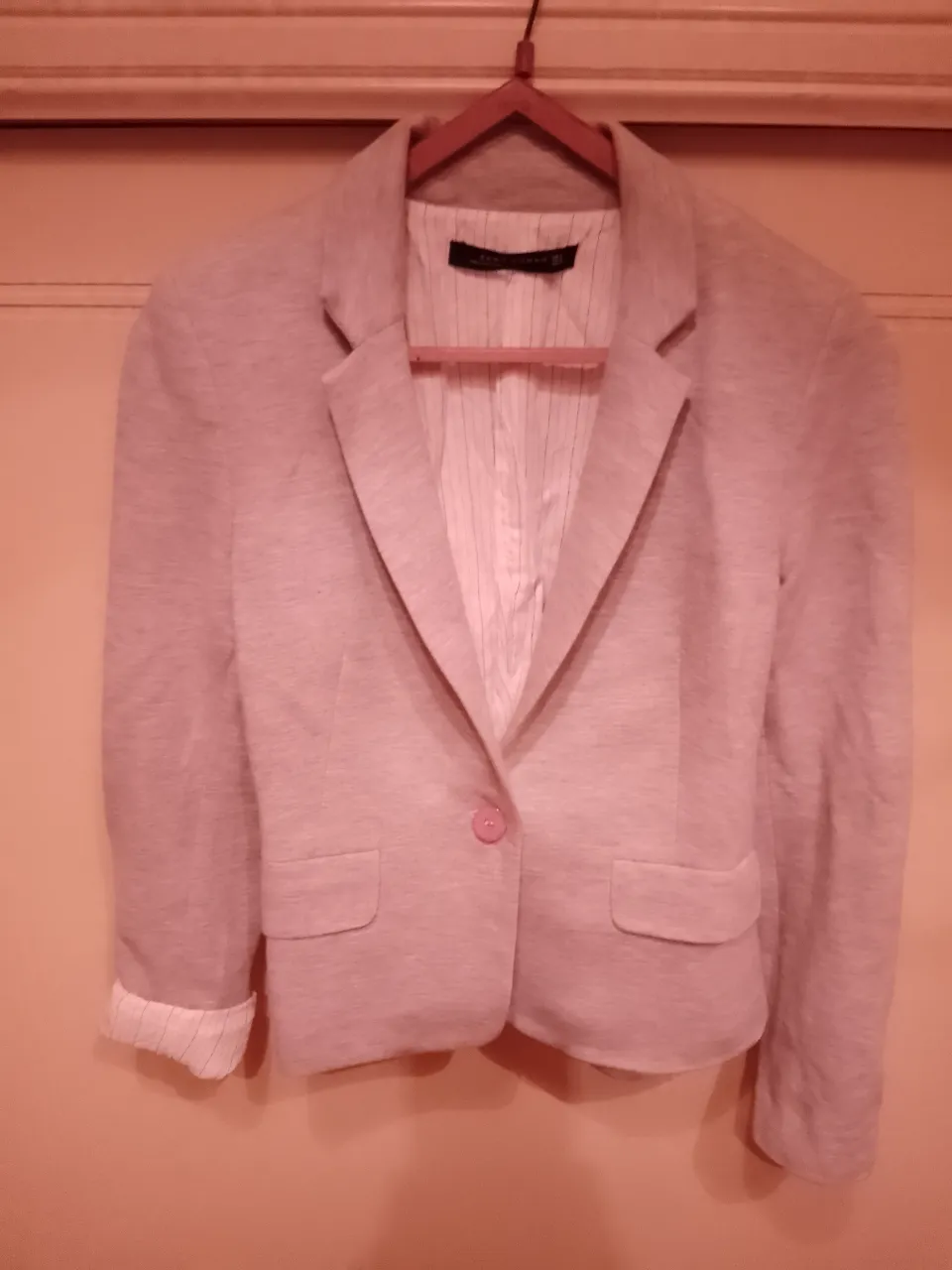Blazer color gris, con un solo botón al frente y detalles de botones en las mangas. Posee un forro a rayas finas. Ideal para un look elegante y moderno.