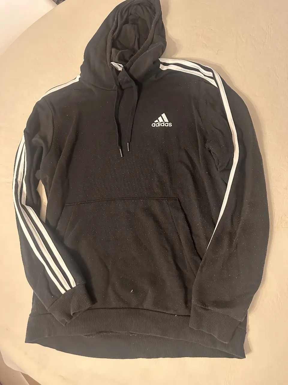 Buzo Adidas negro con las clásicas tres tiras blancas en las mangas y el logo de la marca en el pecho. Ideal para un look deportivo y casual.