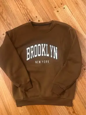 Buzo de cuello redondo color marrón con estampado "BROOKLYN NEW YORK" en blanco. Ideal para un look casual y urbano.