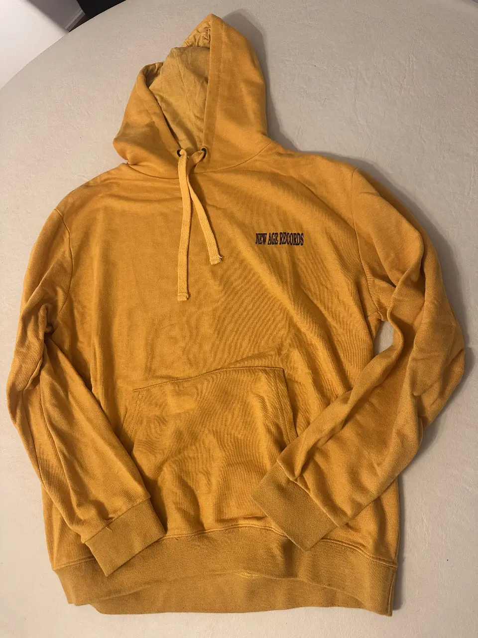Buzo canguro amarillo con capucha y estampado "NEW AGE RECORDS" en la parte delantera y en la espalda "PROUD TO BE STRAIGHT EDGE AYNOT DEAD POISON FREE NEW AGE RECORDS". Ideal para un look urbano y cómodo.