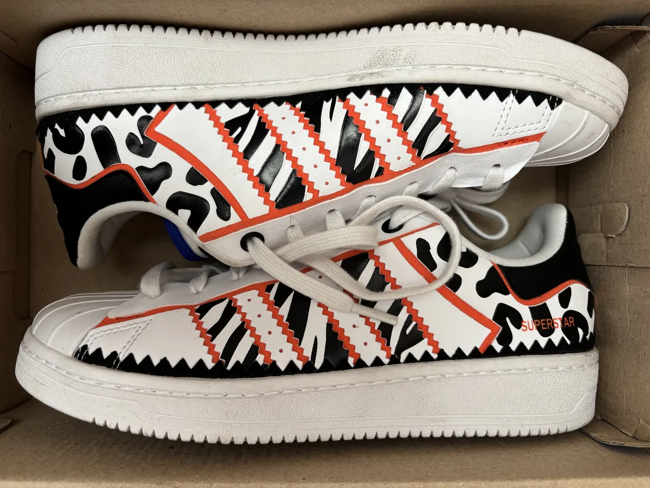 Zapatillas Adidas Superstar con diseño de animal print y detalles en naranja. Ideales para un look urbano y moderno.