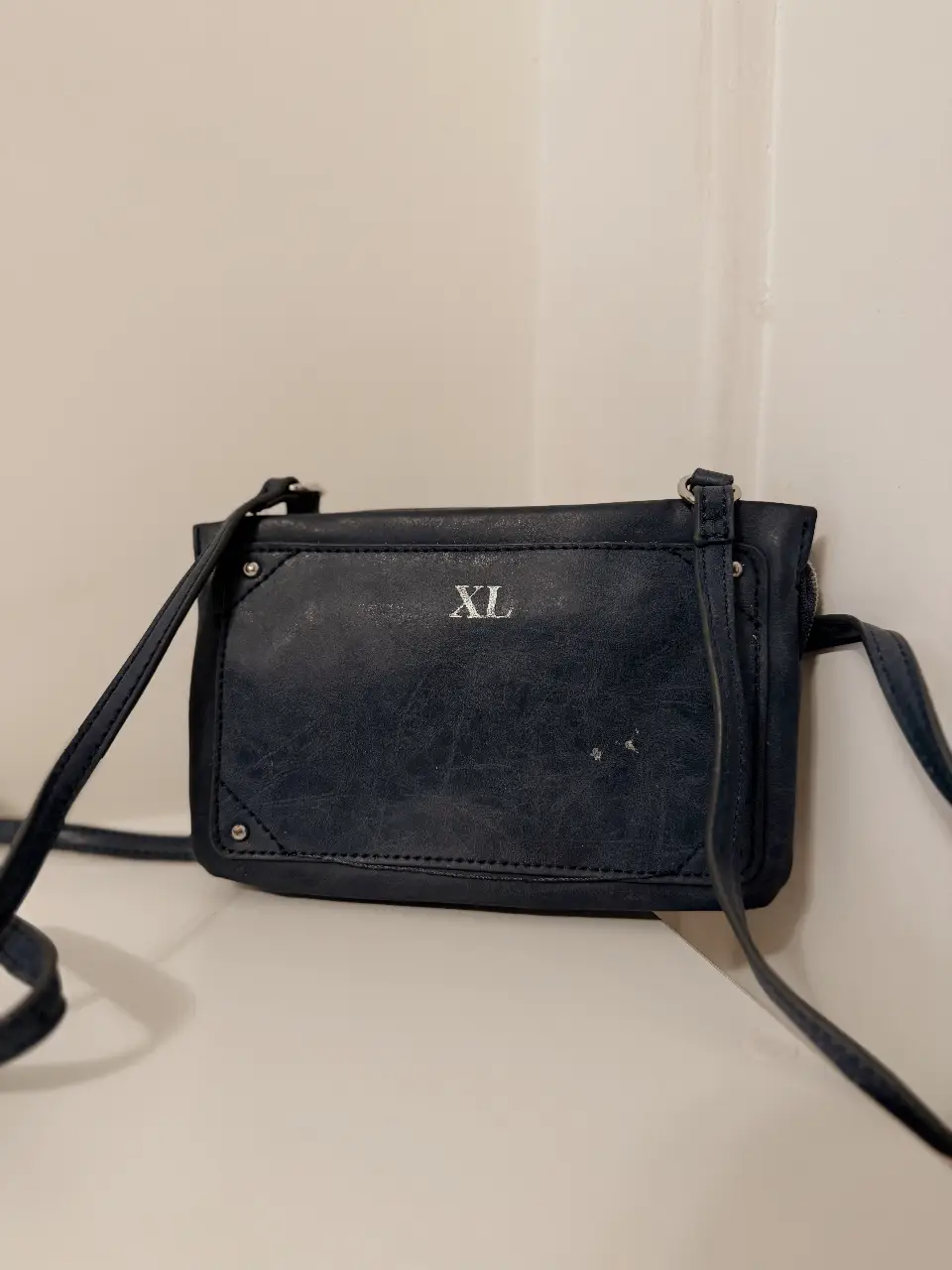 Bandolera azul oscura con detalle "XL" en la parte frontal. Cuenta con cierre y múltiples compartimentos internos. Ideal para llevar lo esencial con estilo.