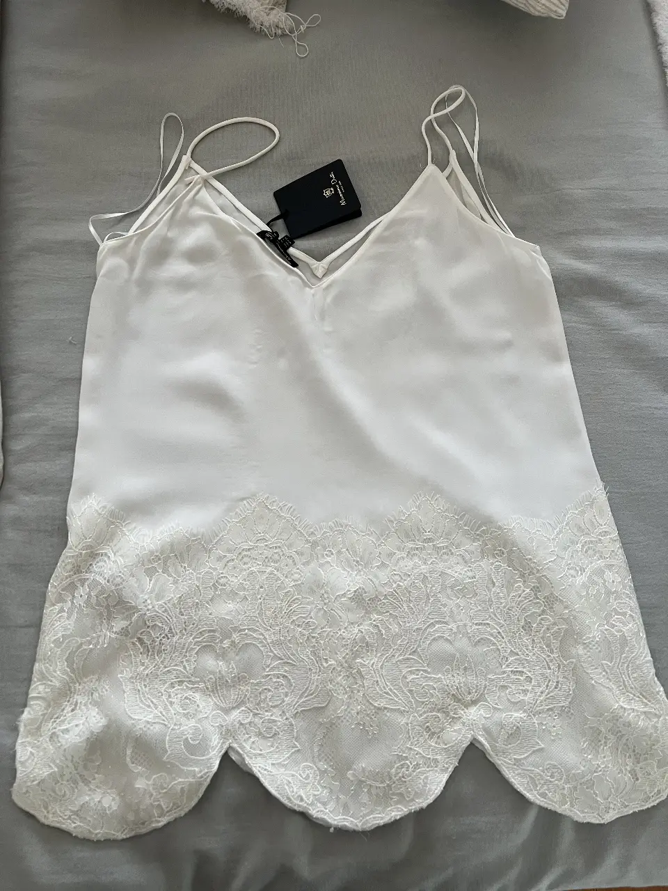 Top de seda blanco con detalle de encaje en el bajo. Ideal para combinar con pantalones de vestir o faldas para un look elegante y sofisticado.