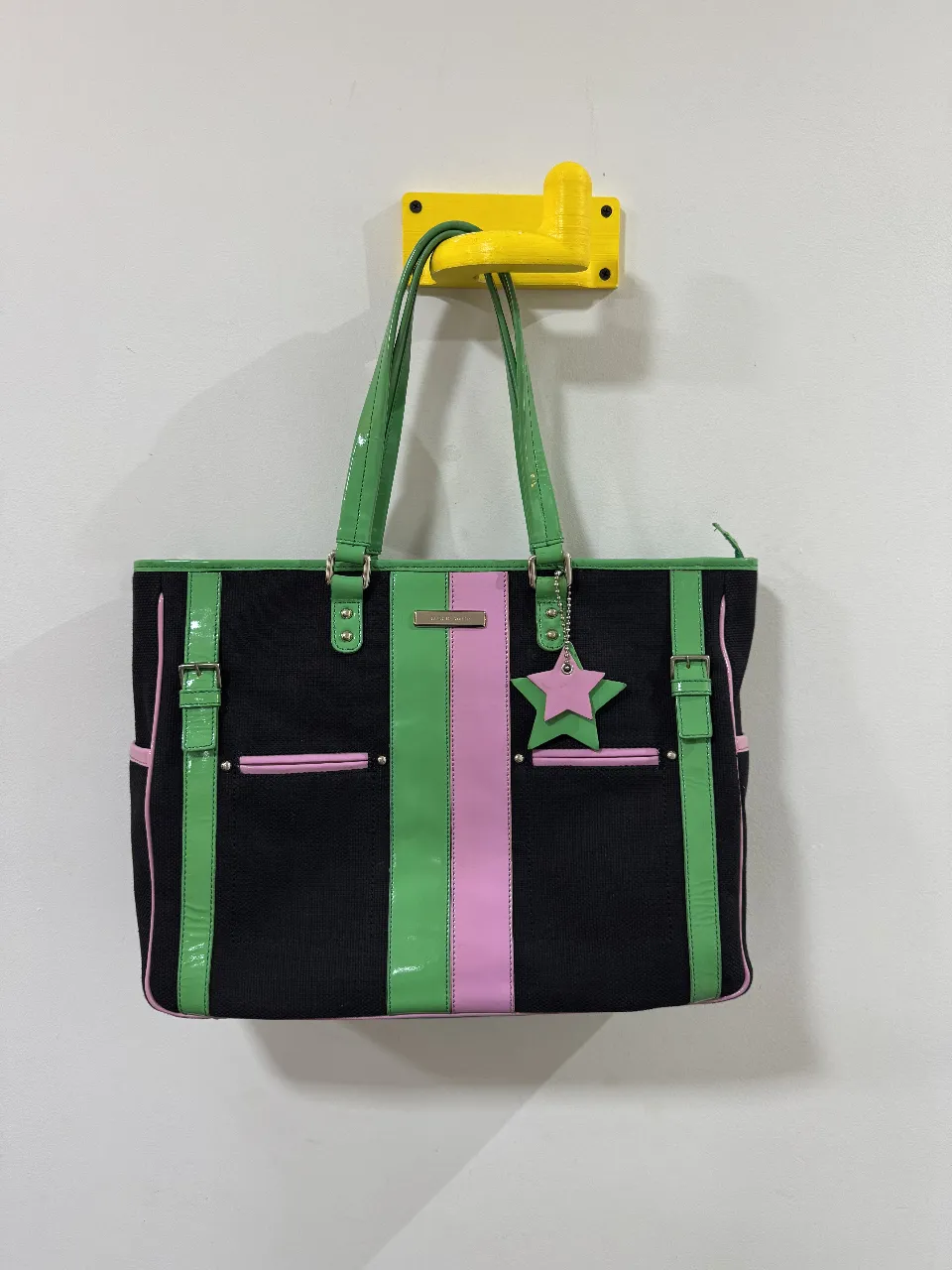 Bolso tote negro con detalles en verde y rosa, ideal para llevar todo lo que necesitas con estilo. Cuenta con manijas y detalles en verde brillante, una franja rosa central y un dije de estrella. Perfecto para un look moderno y funcional. No esta usada, interior levemente desgastado pero sin uso. 