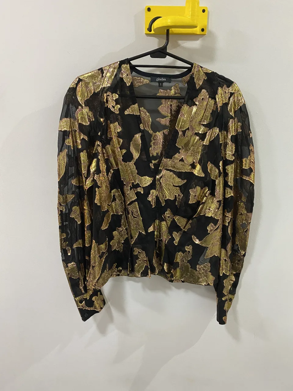 Blusa Ginebra con estampado floral dorado sobre fondo negro, con escote en V y mangas largas abullonadas. Ideal para un look elegante y sofisticado.